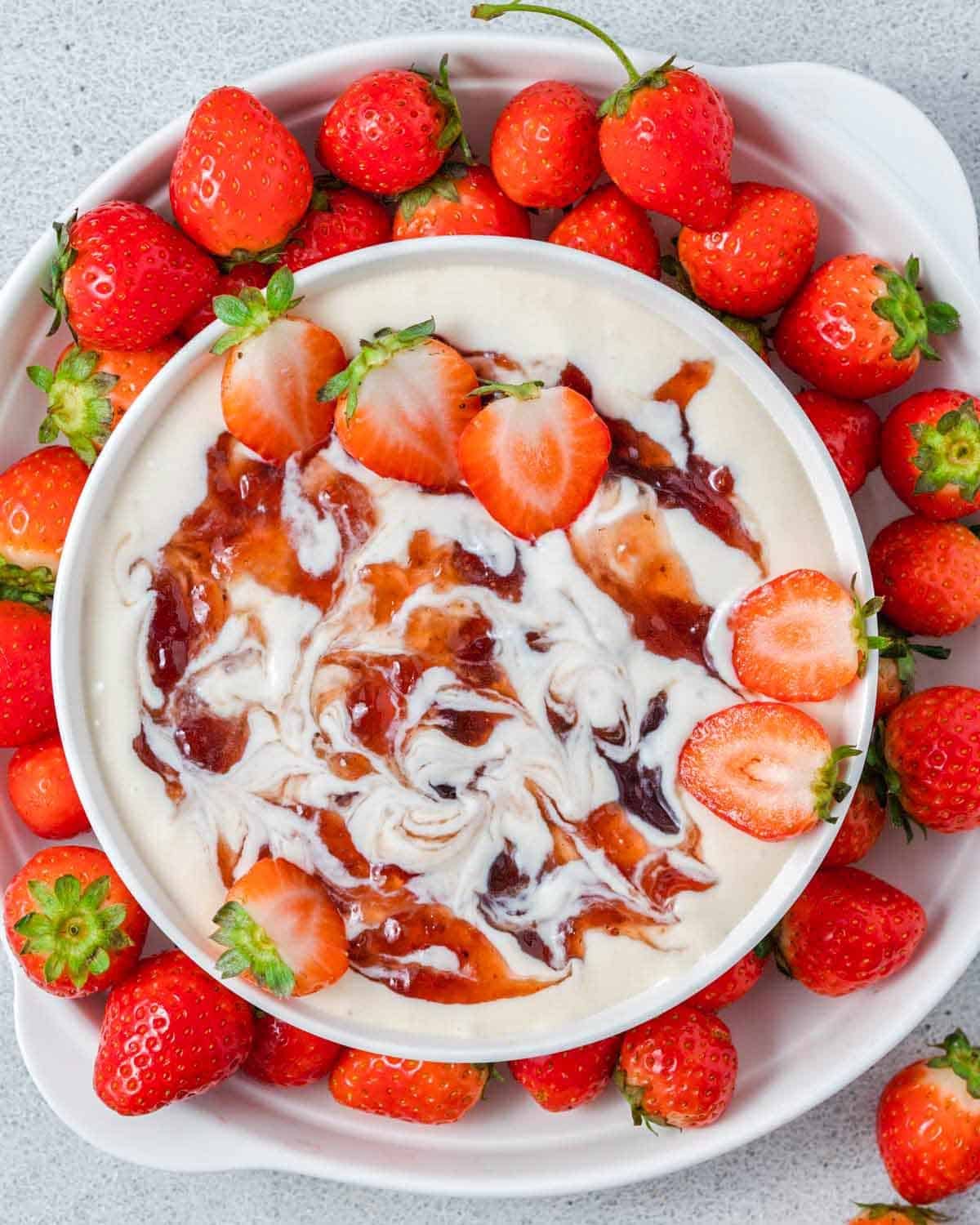a bowl with strawberry fruit dip surrounded by fresh strawberries.