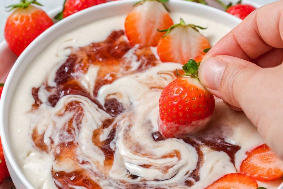 hand dipping a strawberry in a yogurt fruit dip bowl.