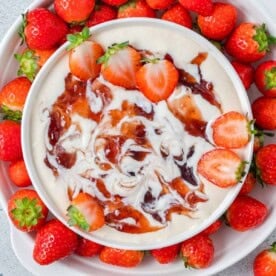 a bowl with strawberry fruit dip surrounded by fresh strawberries.