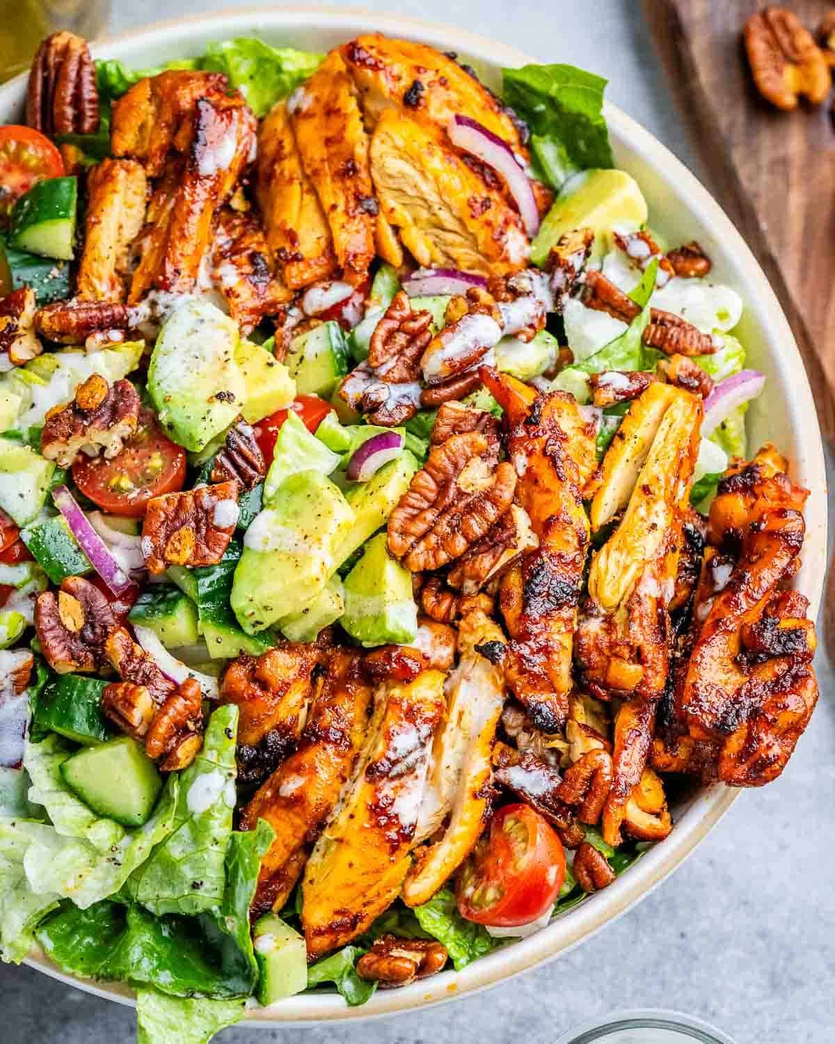 a bowl filled with salad topped with sliced bbq chicken thighs and other veggies.