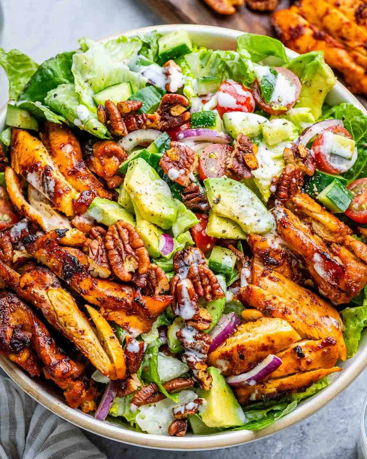 a salad bowl topped with grilled bbq chicken and drizzled with a homemade dressing.