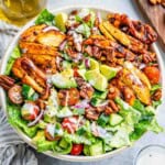 a round bowl of salad topped with sliced BBQ chicken thighs.