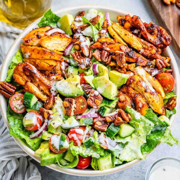 a round bowl of salad topped with sliced BBQ chicken thighs.