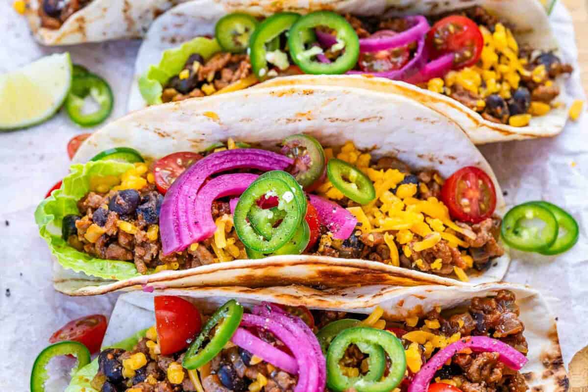 ground beef tacos assembled and topped with pickled onions and sliced jalapenos.