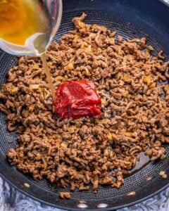 tomato paste added over the ground beef and broth being poured over.