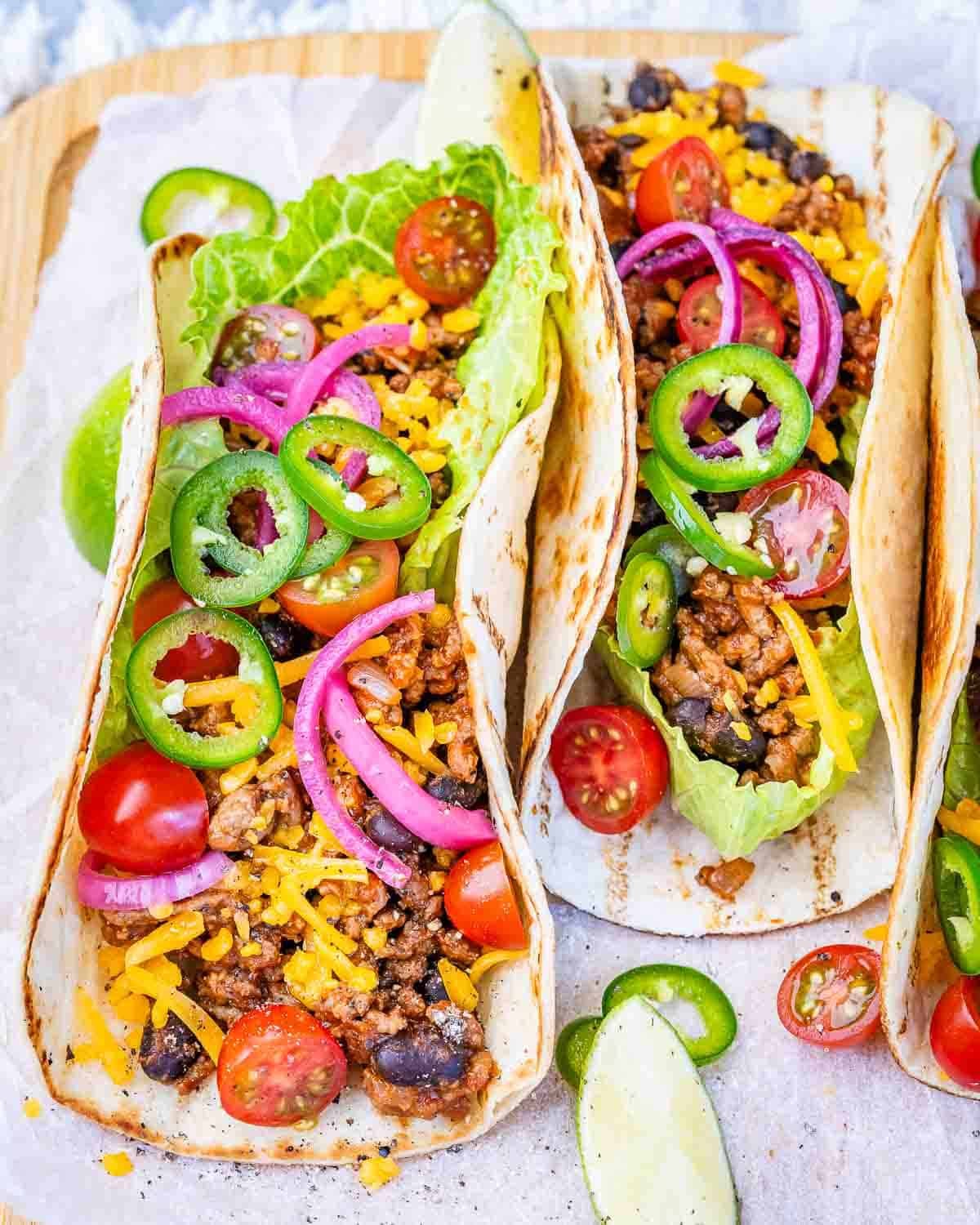 taco filled with ground beef and topped with sliced jalapenos, tomatoes, shredded cheese, and pickled onions. 