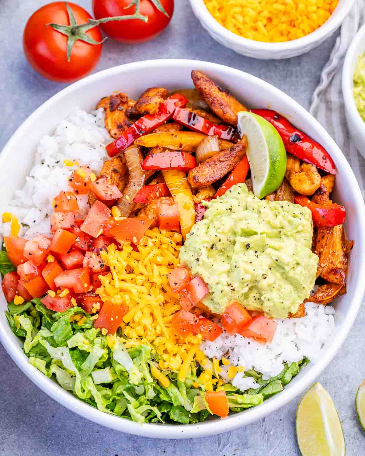 A chicken fajita bowl with avocado, tomato, lettuce and rice.
