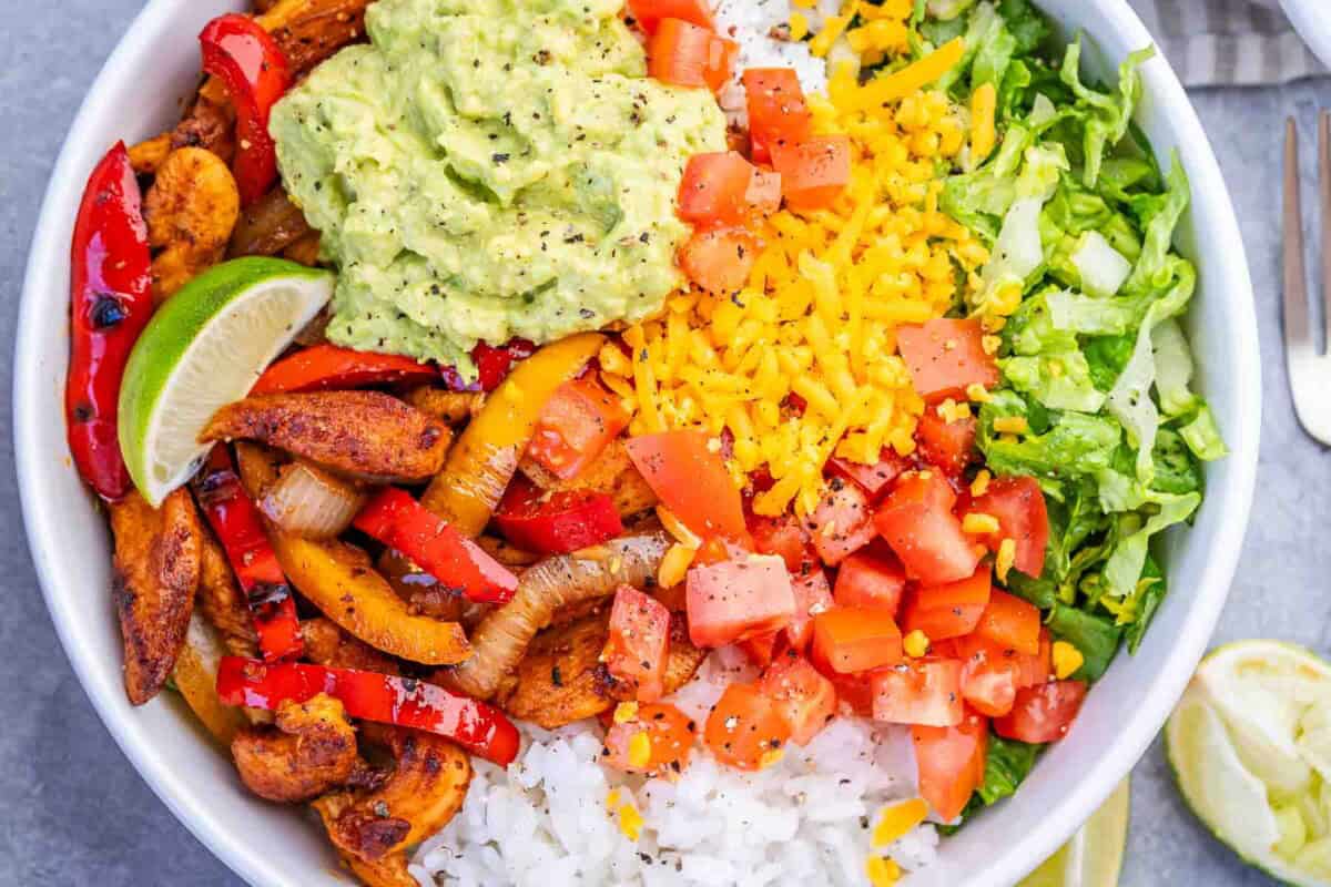 chicken fajita in a bowl with rice, guac, and shredded lettuce.