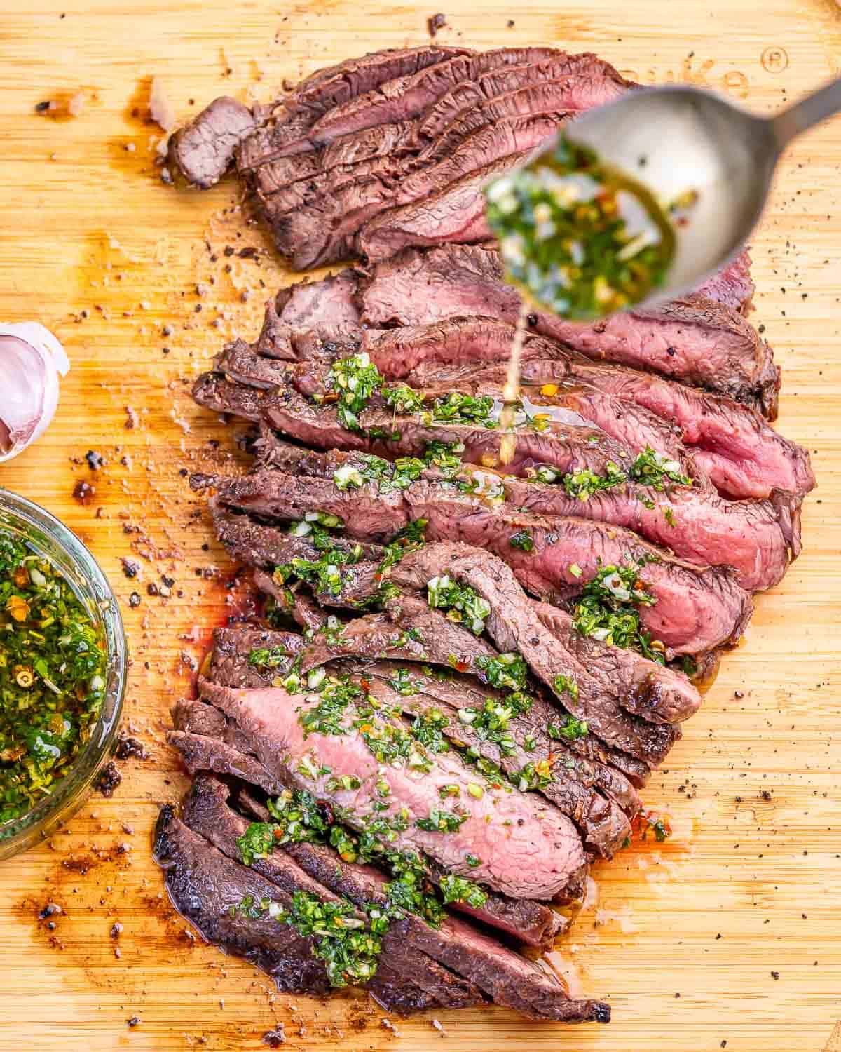 Grilled flank steak being drizzled with chimichurri