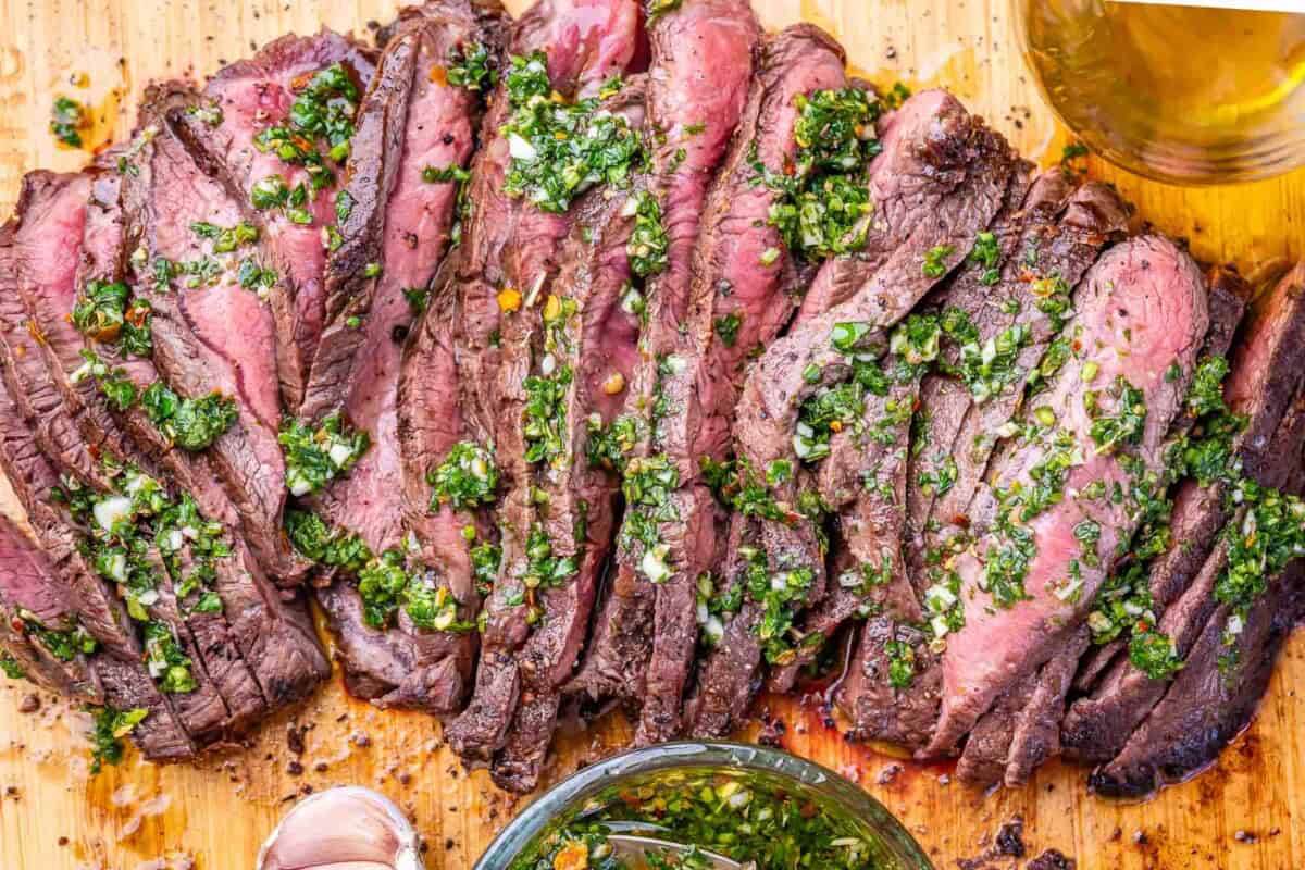 sliced steak on a cutting board topped with chimichurri sauce.