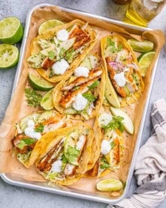 A tray of mahi mahi fish tacos with cabbage slaw and lime wedges.
