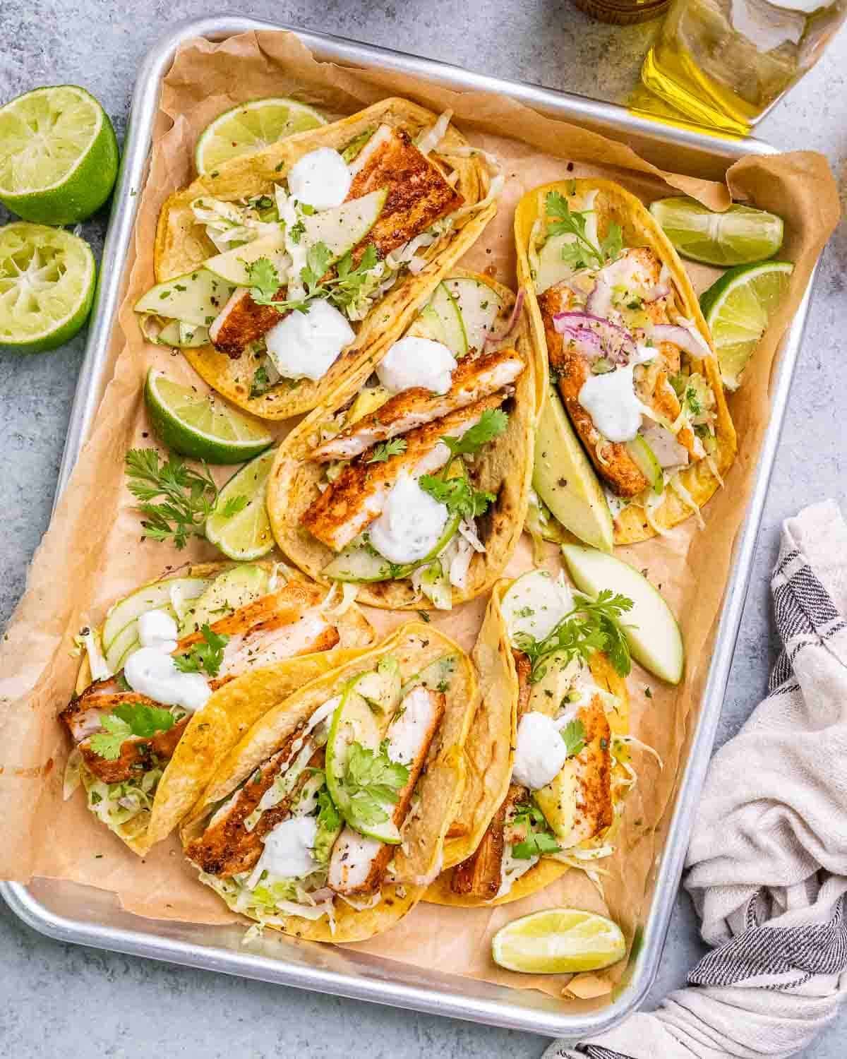 A tray of mahi mahi fish tacos with cabbage slaw and lime wedges.