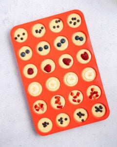 pancake batter in muffin tins topped with fruits.