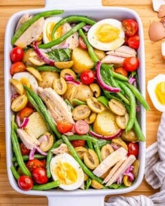 Nicoise salad with eggs, potatoes, olives, green beans and tuna in a white serving dish.