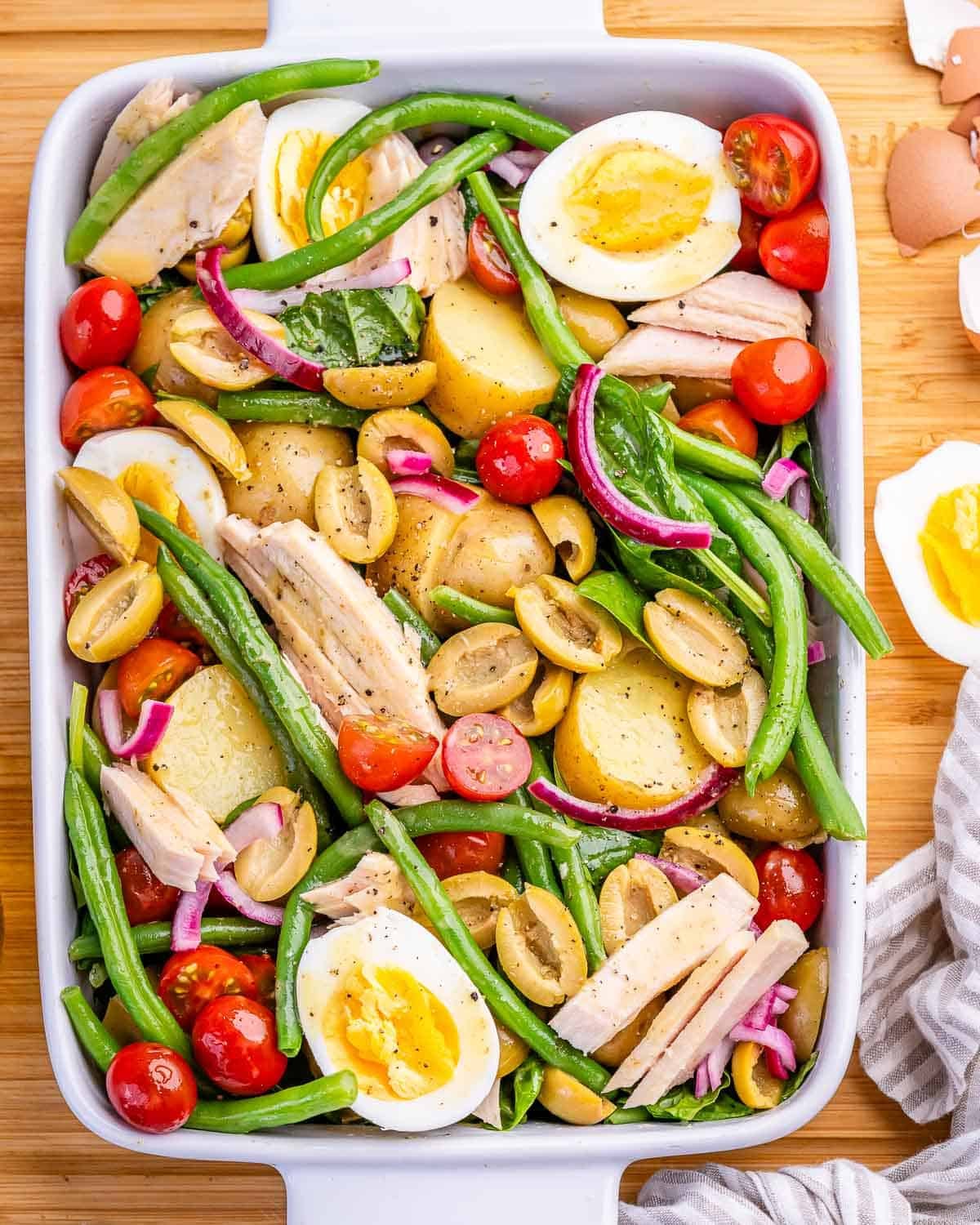 Nicoise salad with eggs, potatoes, olives, green beans and tuna in a white serving dish.