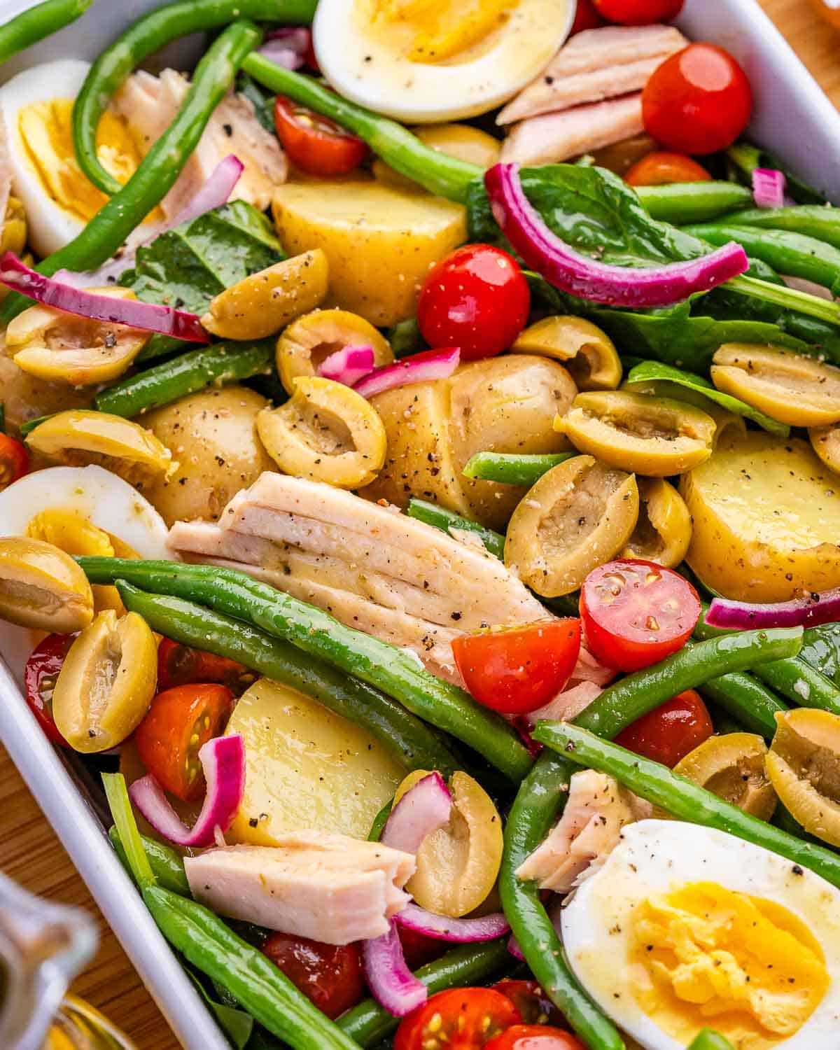 A close up image of Nicoise salad with olives, tuna, potatoes, eggs, green beans and tomatoes.