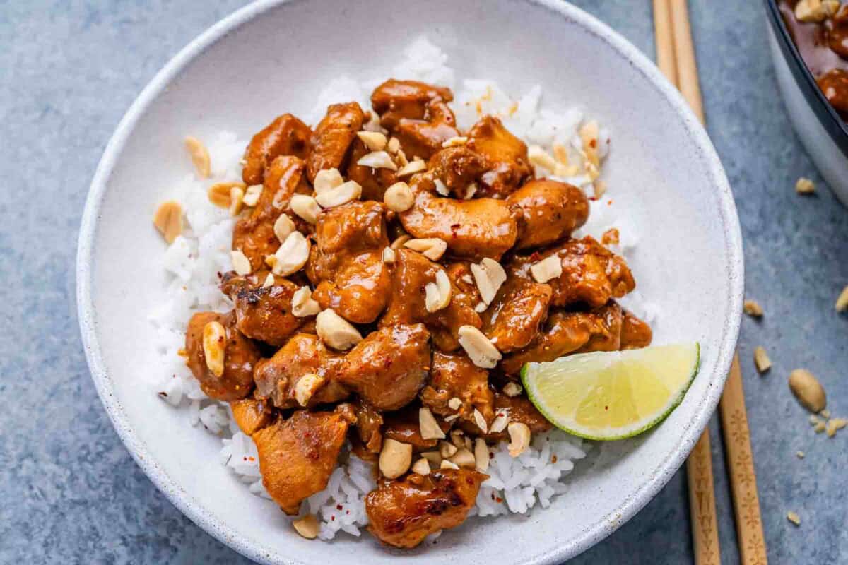seared chicken in peanut butter sauce added over white rice in a bowl.