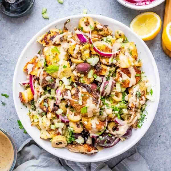 potato salad in a white bowl with veggies, olives, and dressing.