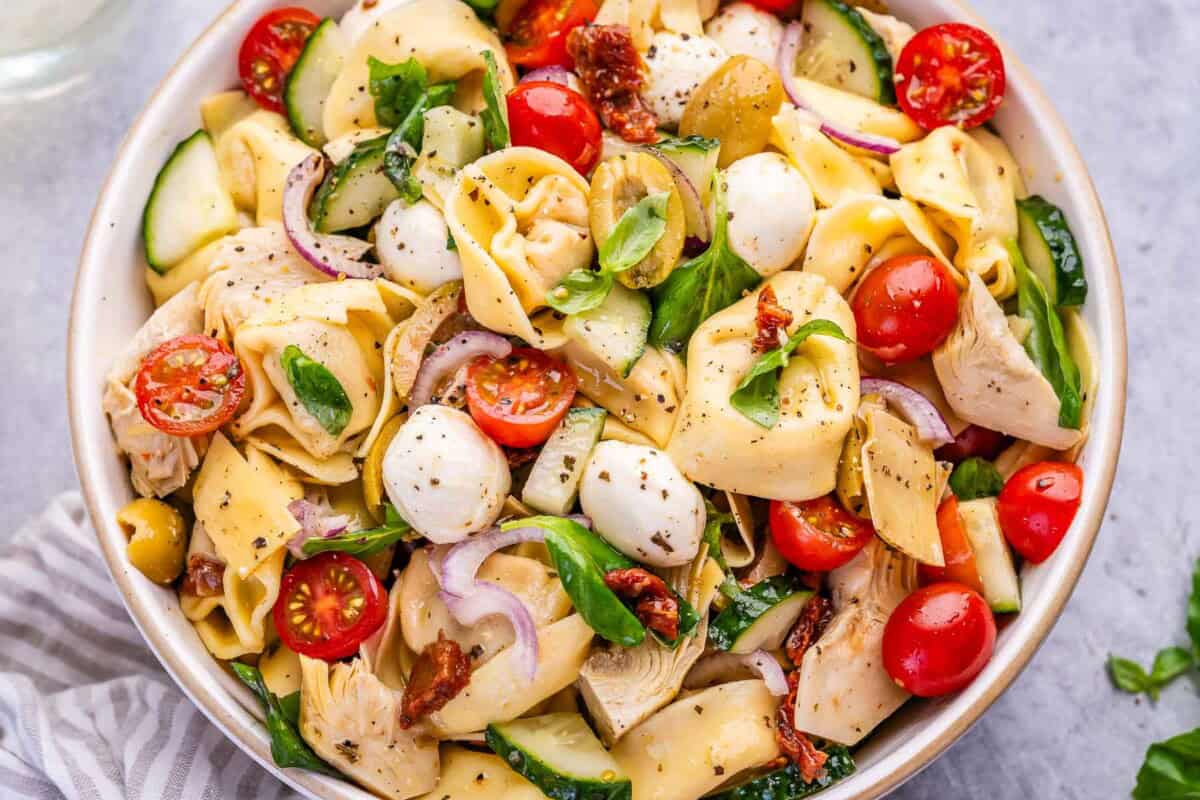 tortellini pasta salad in a bowl with veggies and mozzarella pearls.