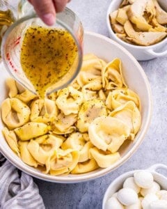 dressing being poured over the tortellini pasta.
