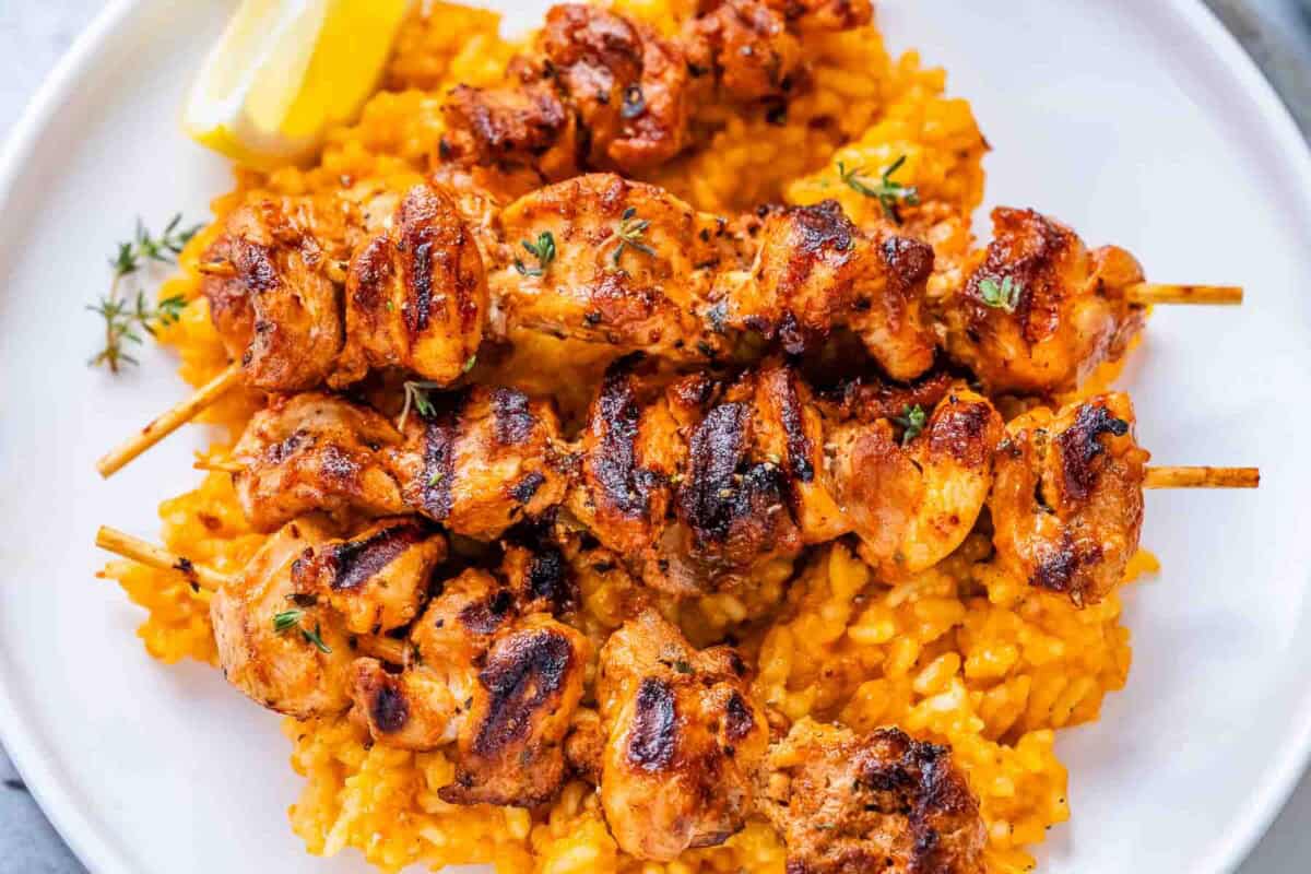 marinated grilled chicken skewers served over a plate of rice.