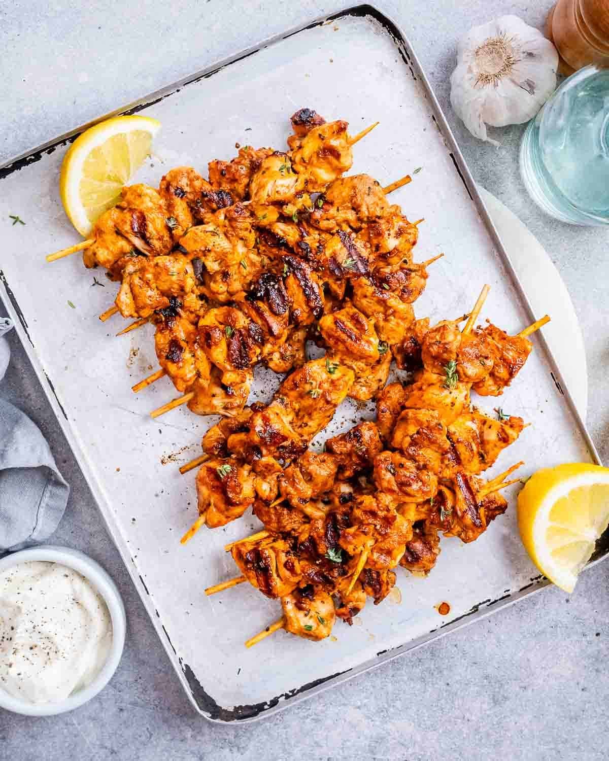 Yogurt marinated chicken on a sheet pan with lemon wedges.