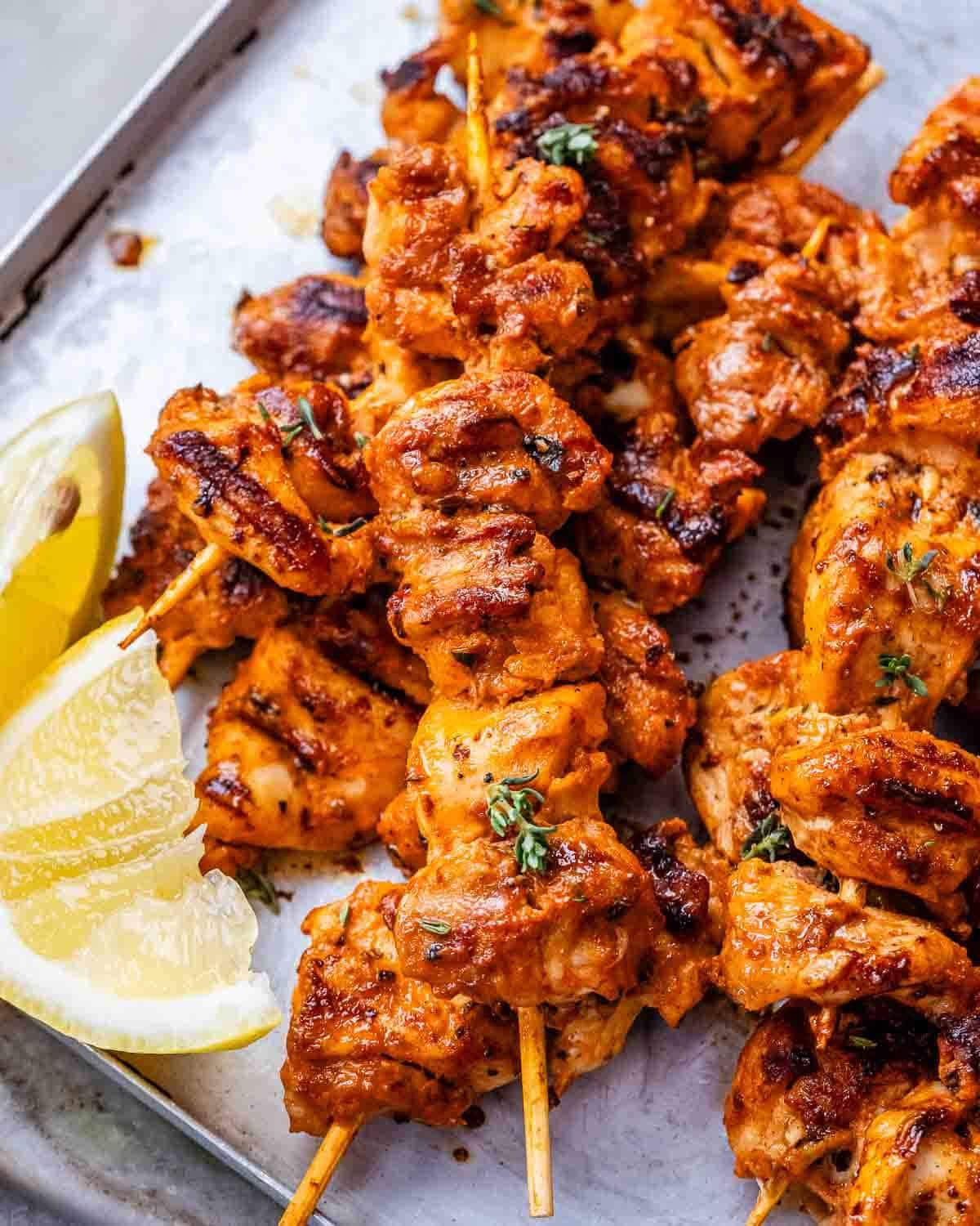 A close up of yogurt marinated chicken on skewers with lemon wedges.