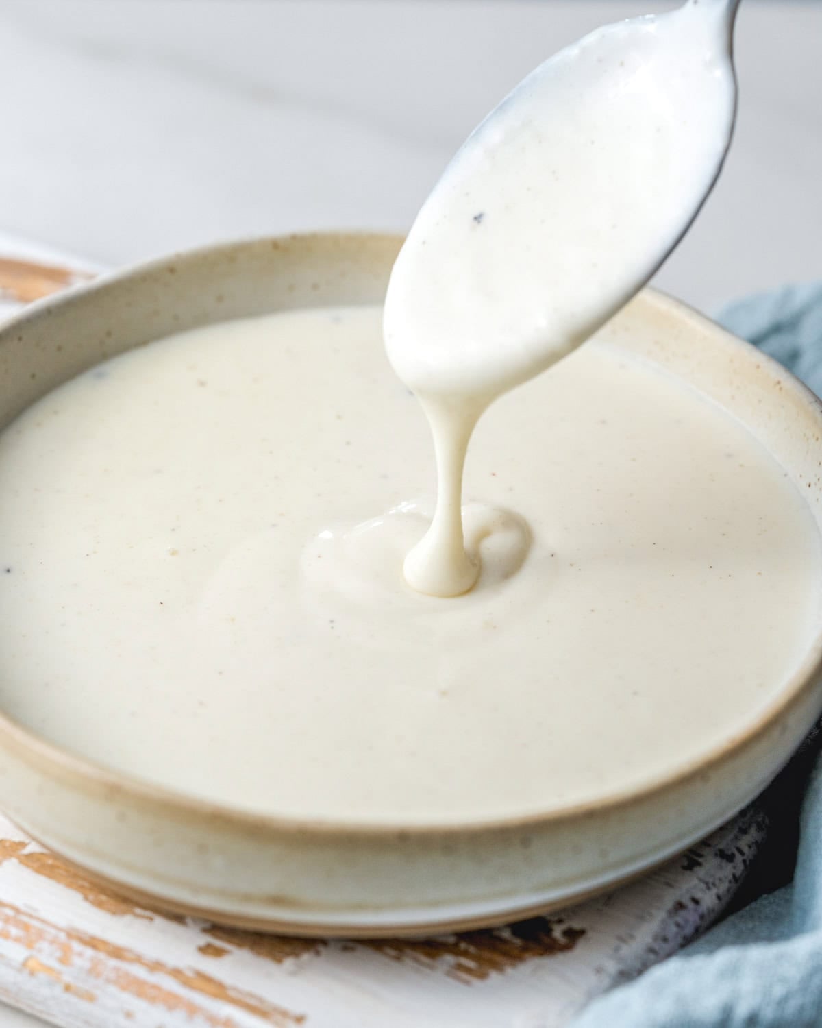 a bowl with bechamel sauce and a spoon dipped in the sauce.