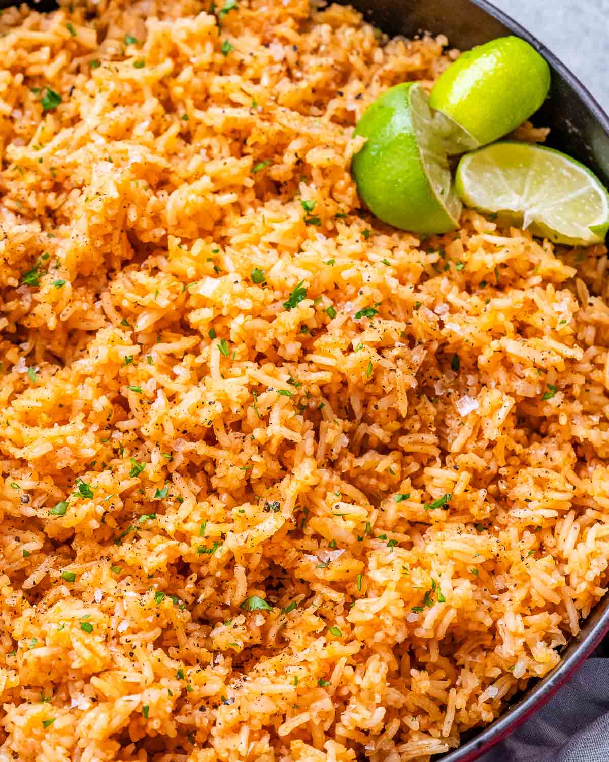 A skillet of Mexican rice with lime wedges.