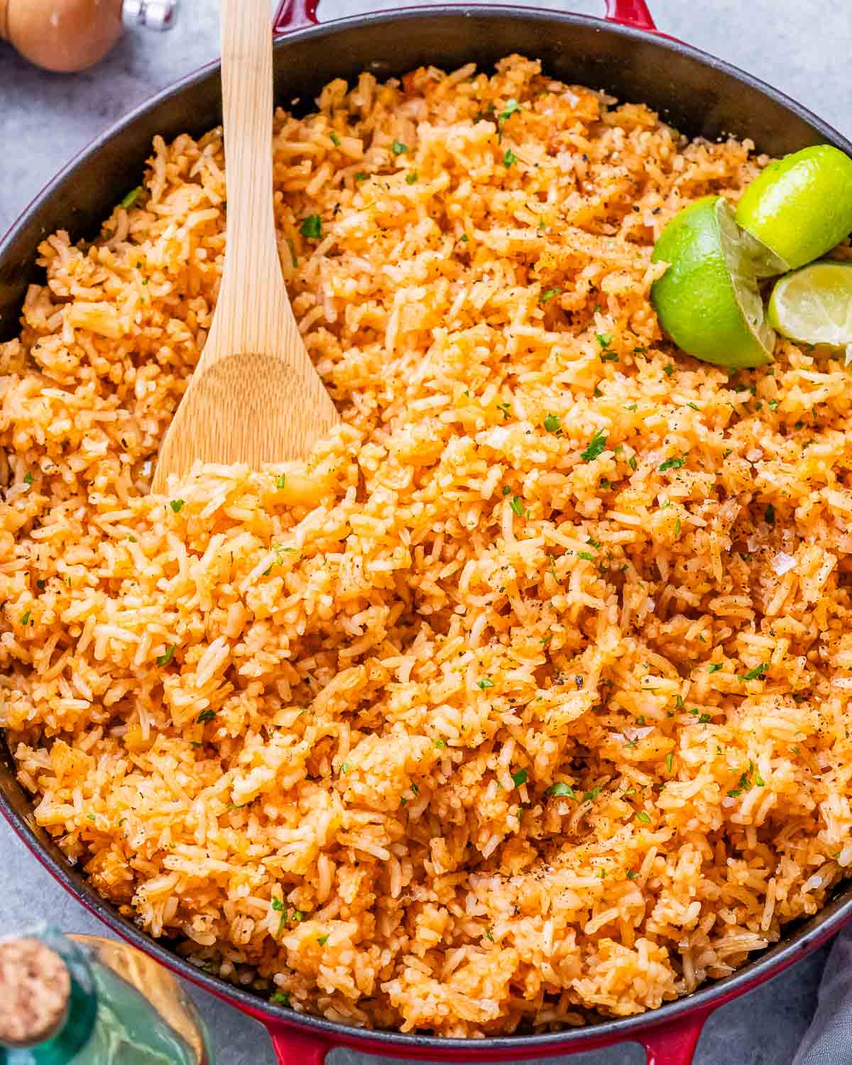 Mexican rice in a skillet with a wooden spoon and lime wedges.