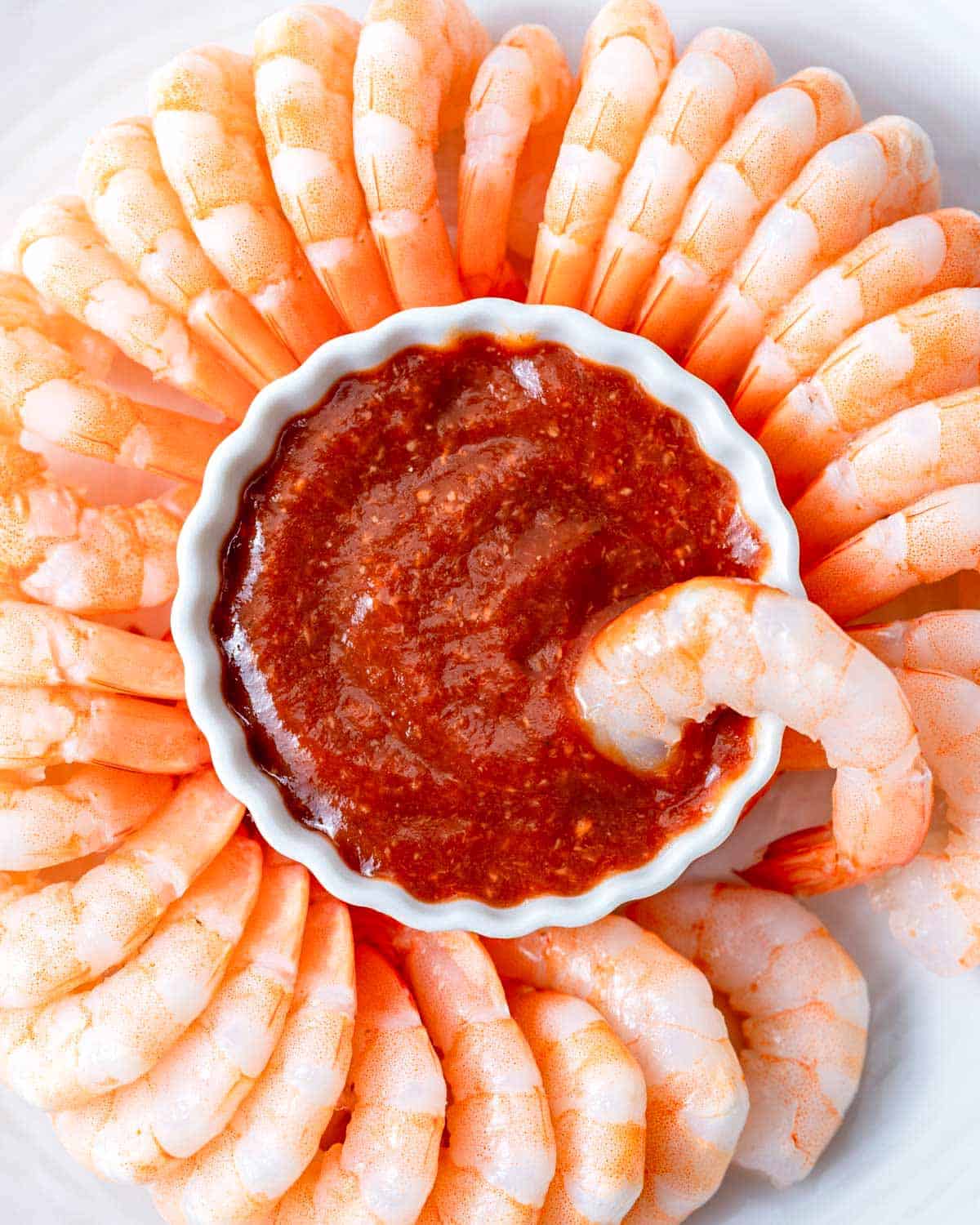 a bowl of homemade cocktail sauce surrounded by cooked cold shrimp.