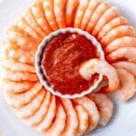 a bowl of cocktail sauce surrounded by cooked shrimp.
