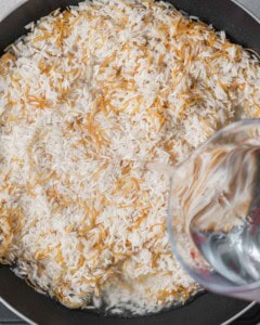 adding water over the rice in a pan.