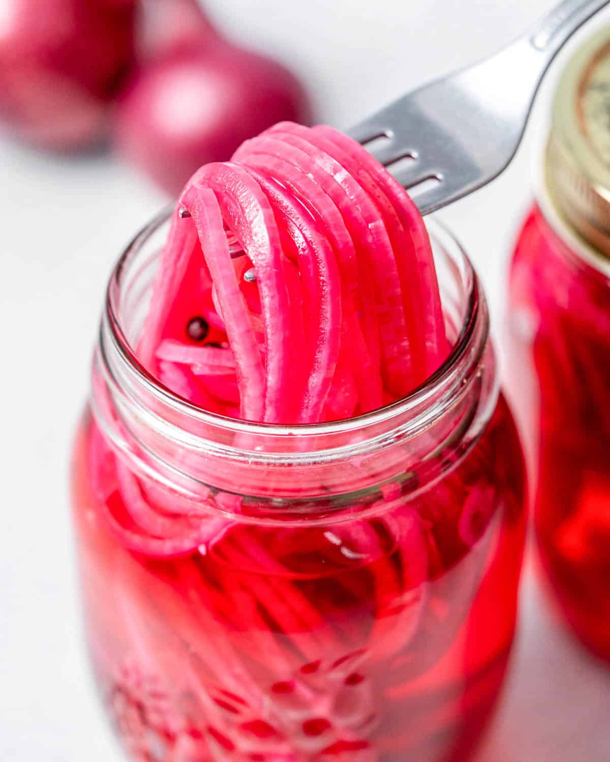 pickled red onions in a jar with fork grabbing some from the jar.