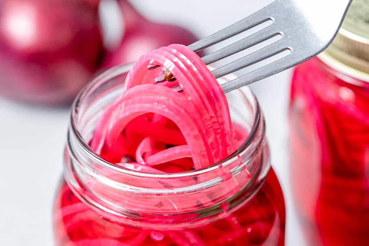 fork grabbing pickled red onions in a jar.