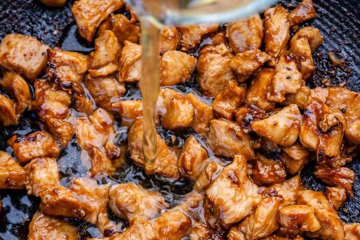 pouring broth over bbq chicken in a pan.