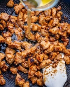 adding broth over cooked bbq chicken in a skillet.