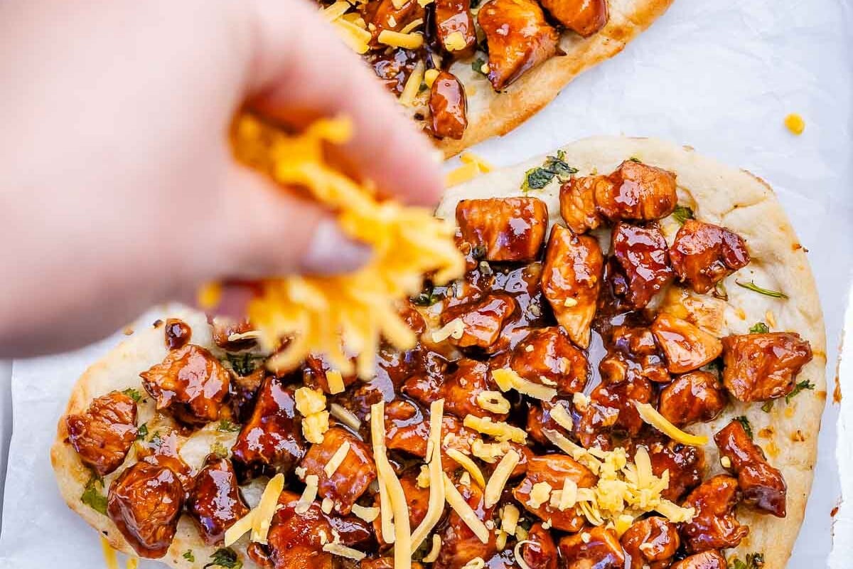 adding shredded cheese over bbq chicken flatbread.