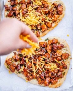 adding shredded cheese over the bbq chicken over the naan.
