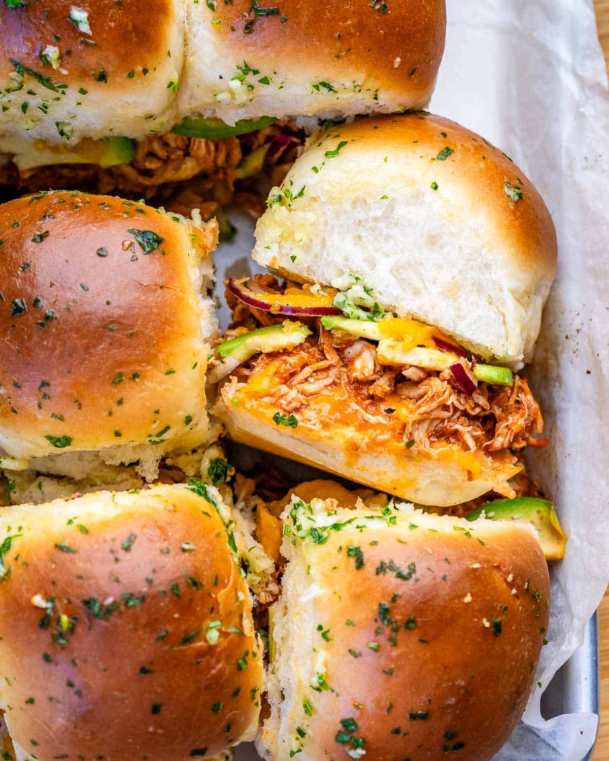 BBQ chicken sliders with avocado in a parchment-lined tray.