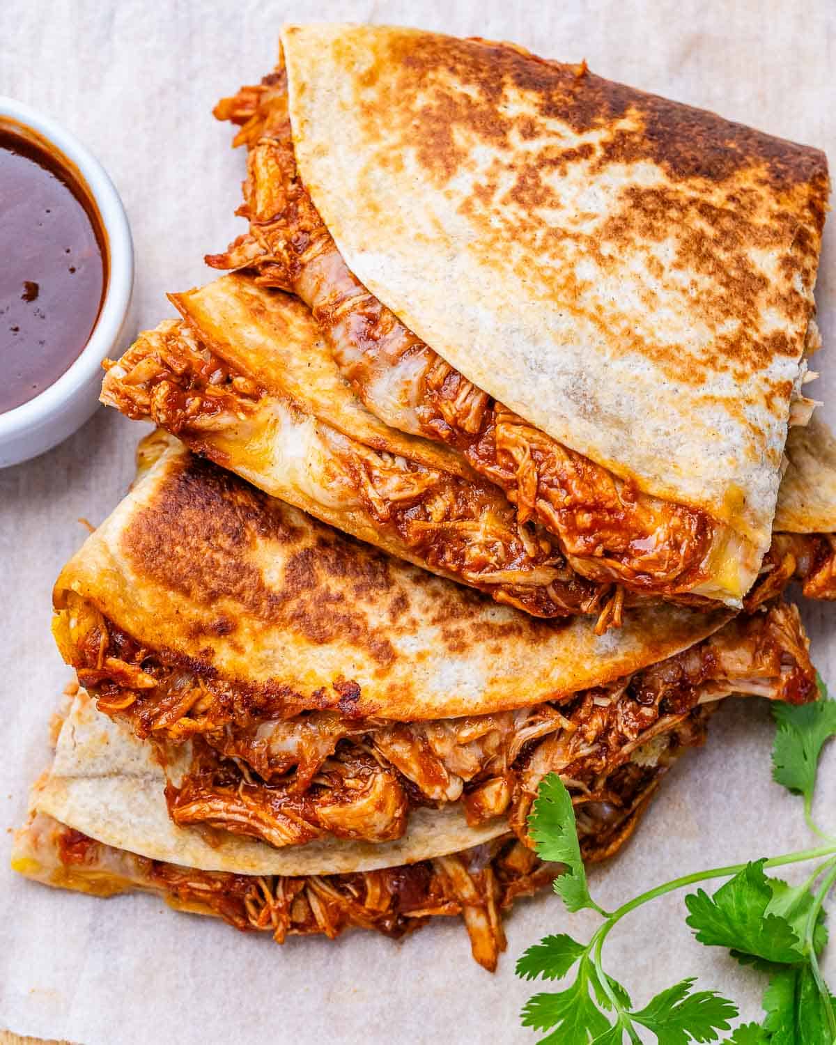 Copycat chipotle chicken quesadillas on parchment paper with a sprig of cilantro.