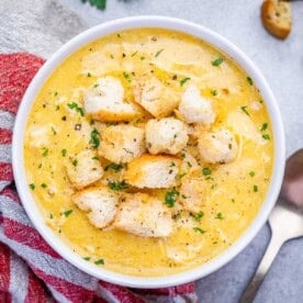 a round white bowl filled with cream of chicken soup topped with croutons.