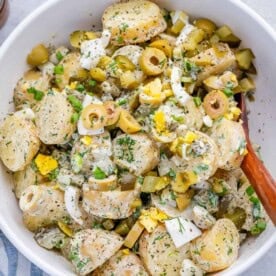 a white bowl with potato salad made with pickles and fresh dill.