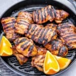 chicken thighs grilled in a grill pan with orange wedges.
