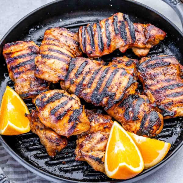 chicken thighs grilled in a grill pan with orange wedges.
