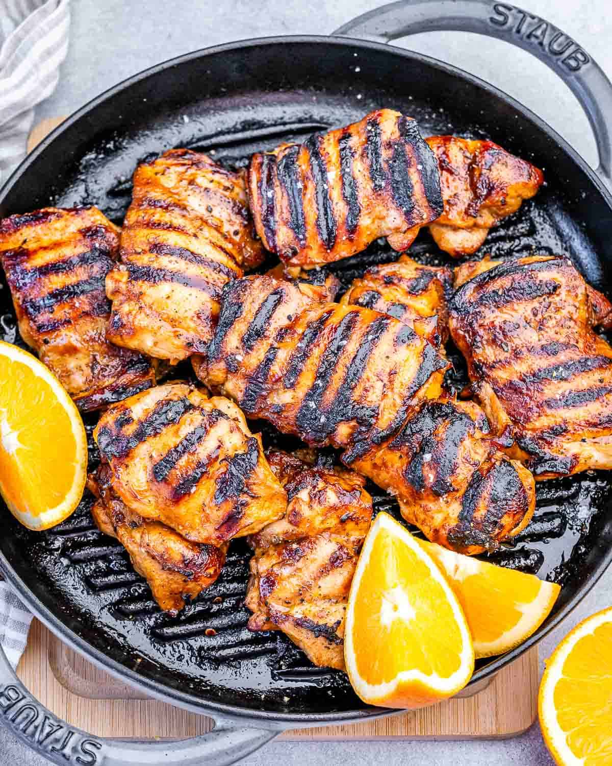 a grill pan with grilled chicken thighs and orange slices as garnishes.