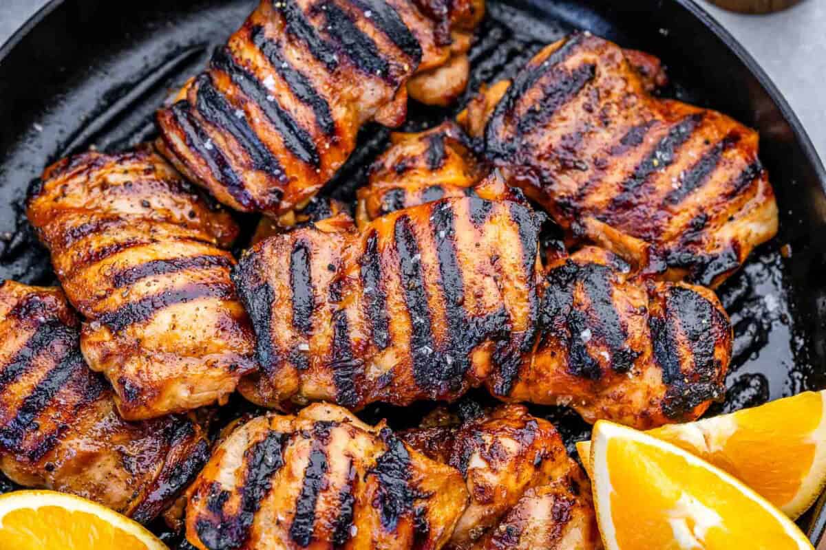 grilled chicken thighs on a pan with slices of oranges next to them.