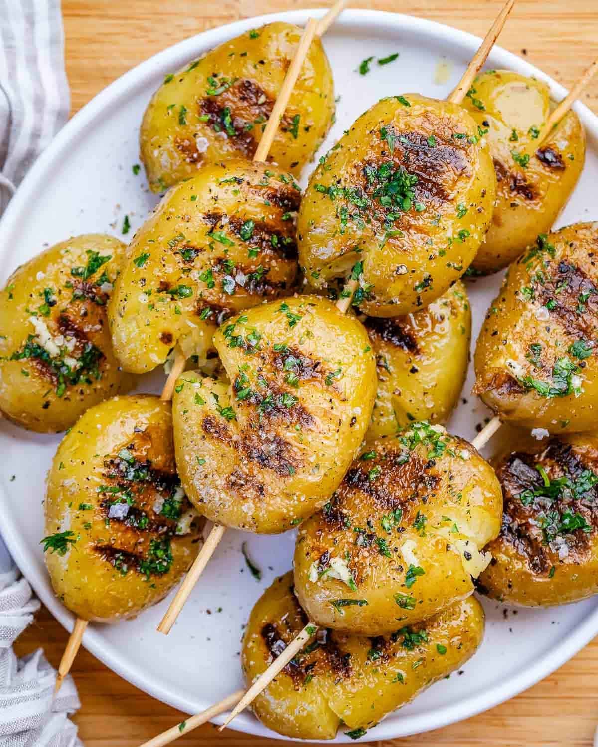 A white plate of grilled potatoes brushed with garlic parsley sauce.