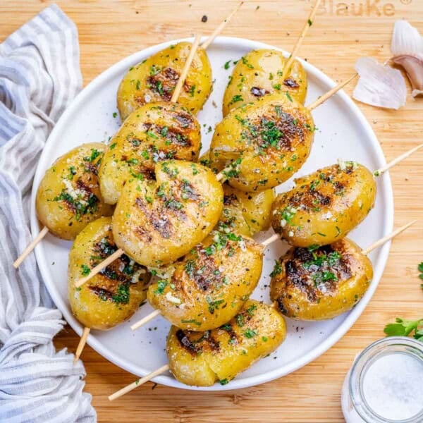 grilled baby yellow potatoes in wooden skewers over a plate.