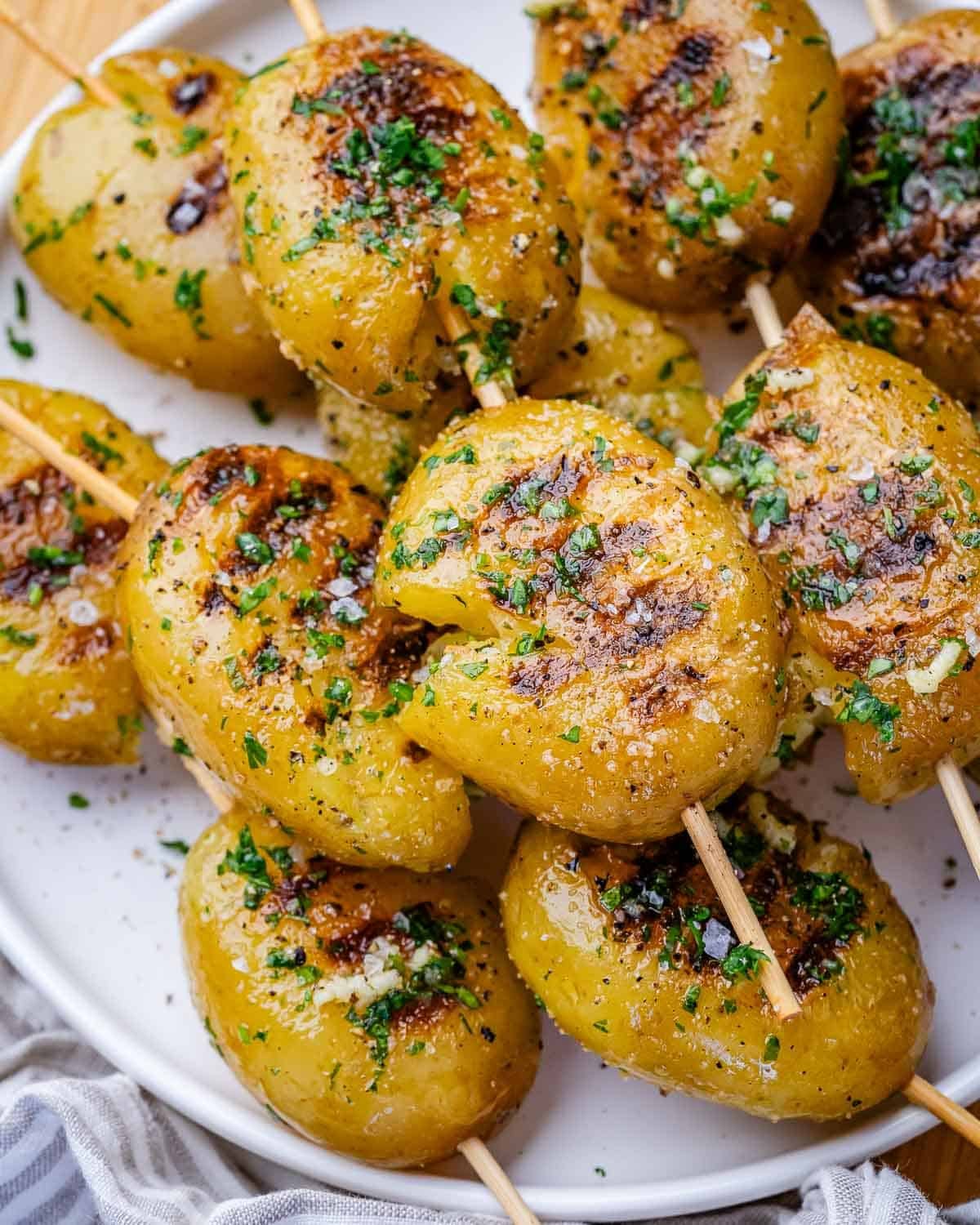 Grilled baby potatoes on skewers on a round white plate